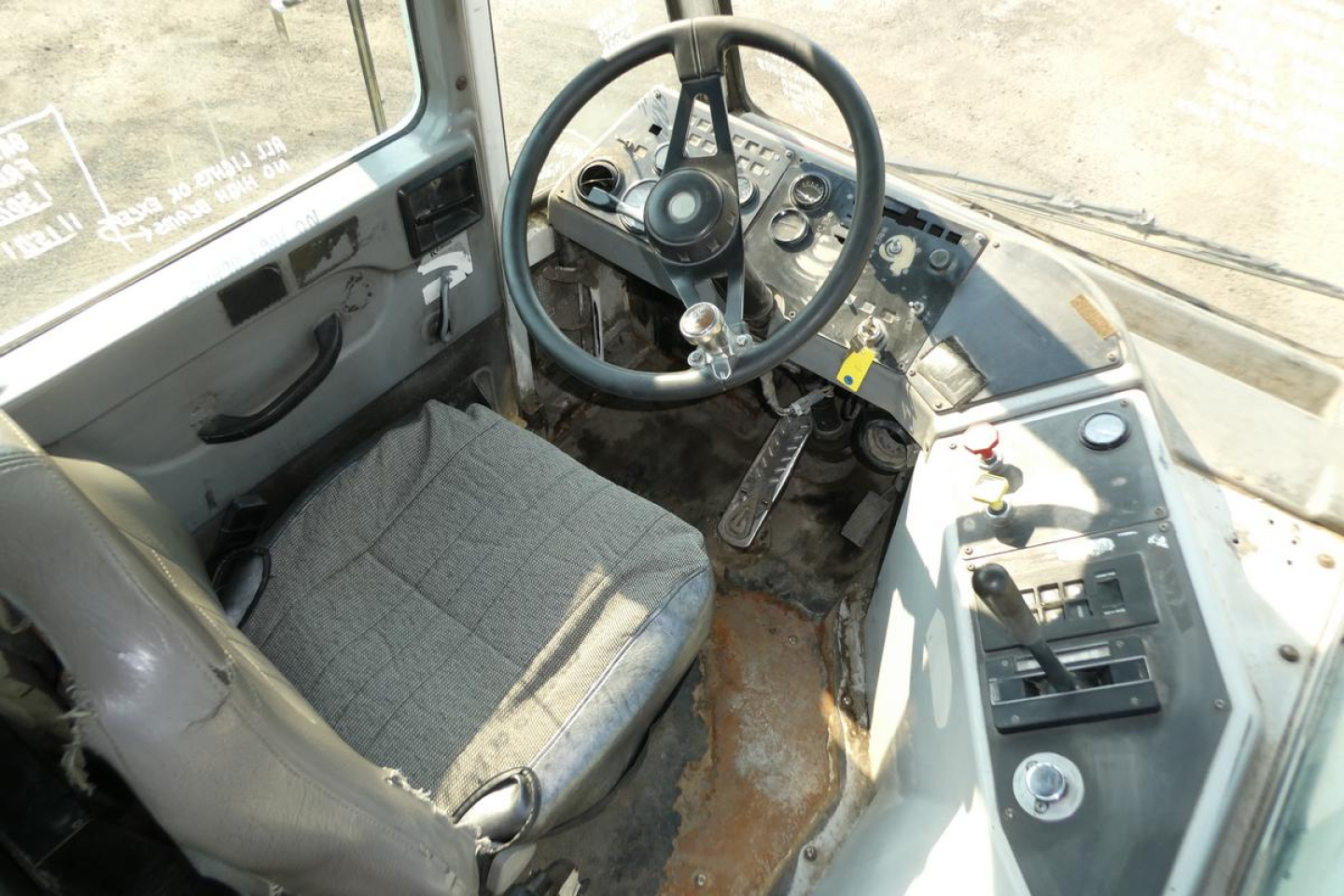 Operator cab of Kalmar Ottawa YT30 with steering wheel, dashboard controls, and gray fabric seat; visible wear on floor and pedals.