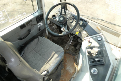 Operator cab of Kalmar Ottawa YT30 with steering wheel, dashboard controls, and gray fabric seat; visible wear on floor and pedals.