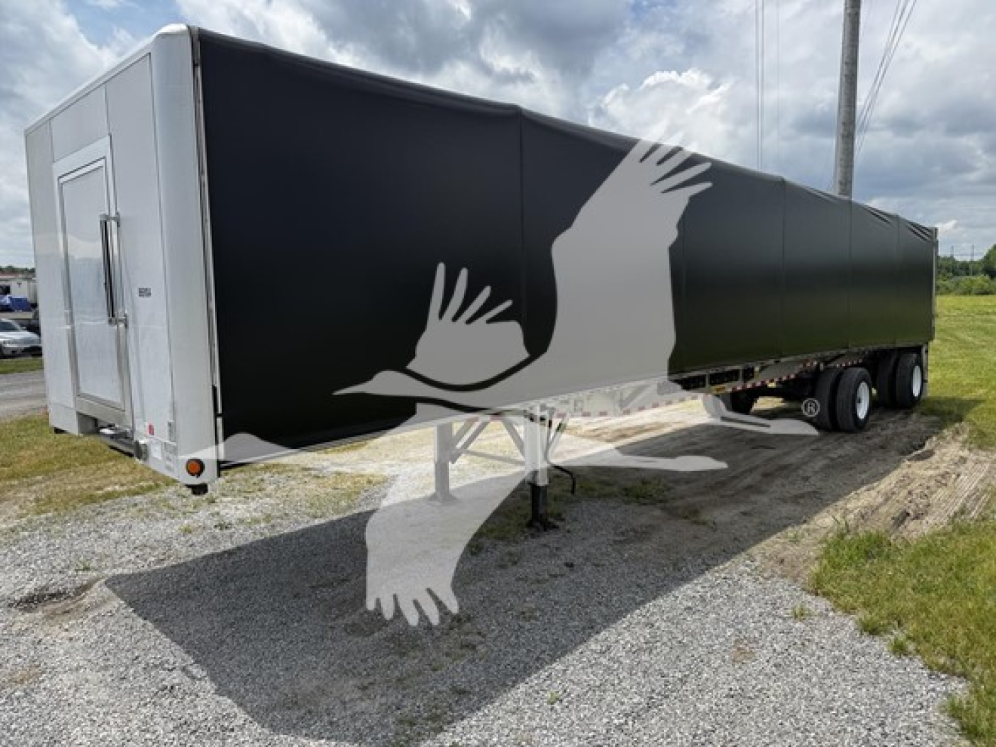 2018 Reitnouer Big Bubba curtainside trailer with black side panel and white rear end, three-axle configuration, in a gravel lot.