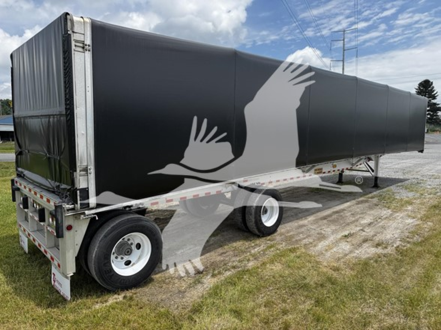 Trailer side showing black curtainside with white graphic birds, rear dual axle, metal frame, tires. No legible labels visible.