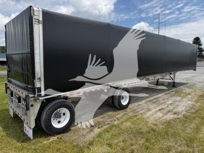 Trailer side showing black curtainside with white graphic birds, rear dual axle, metal frame, tires. No legible labels visible.