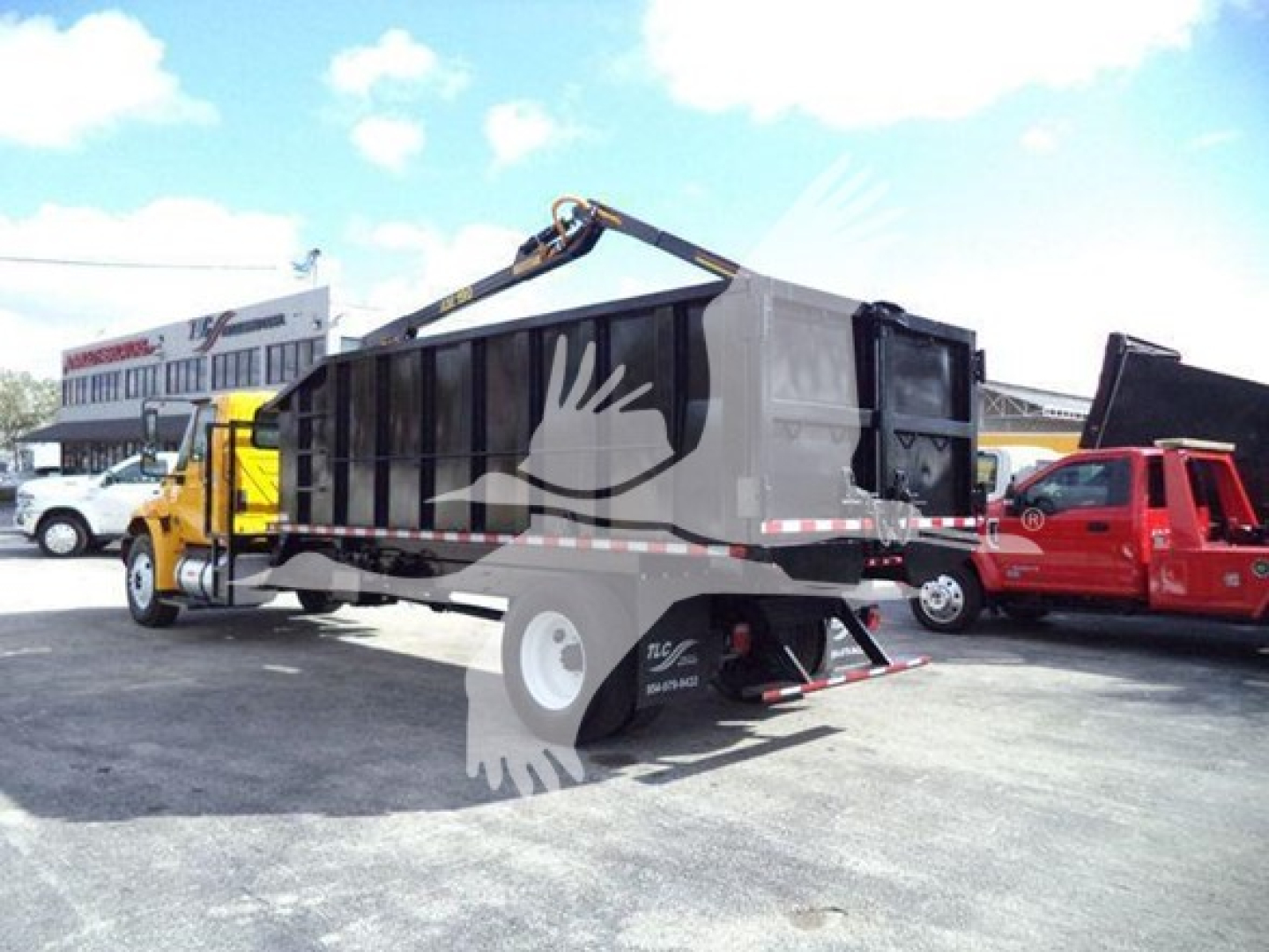 Truck bed with grapple attachment on back of 2019 International Durastar, used; side view showing dump truck with grapple arm and black container.