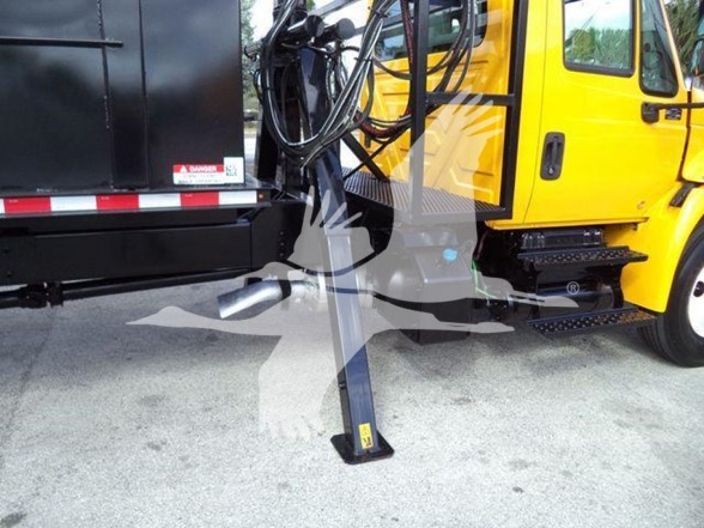 Joystick-style grapple truck with yellow cab and black grapple/boom, side view showing stabilizer leg extended, hoses and control area visible.