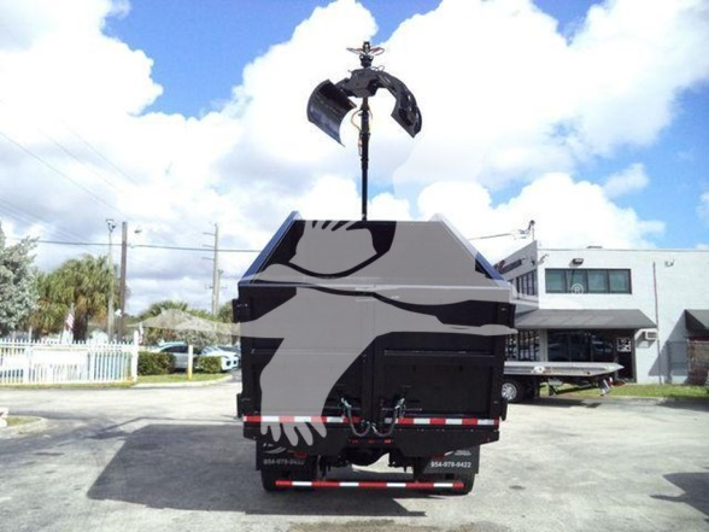 Vehicle rear view showing grapple truck bed and hydraulic claw lifting attachment.