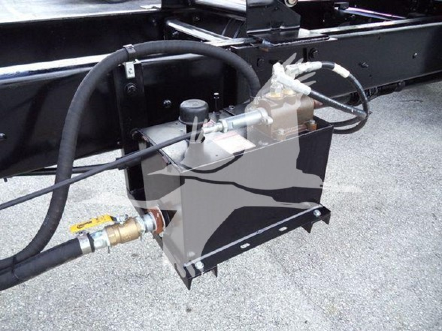 Truck undercarriage showing hydraulic control valve and reservoir with hoses and fittings.
