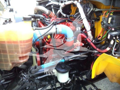 Truck engine bay showing coolant reservoir, blue radiator hose, red engine components, and various hoses in a yellow-framed International Durastar grapple truck.