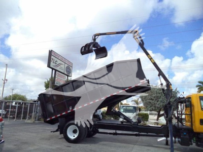 Truck bed with grapple crane attached, 2019 International Durastar, side view showing crane arm, loading grapple, and trailer bed in a yard.