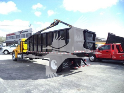Truck bed with grapple attachment on back of 2019 International Durastar, used; side view showing dump truck with grapple arm and black container.
