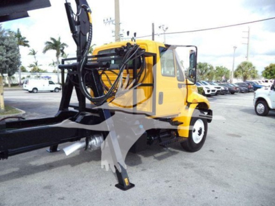 Grapple truck, yellow International Durastar, with cab and front wheels visible, hydraulic boom and grappling arm extending from the rear, in a dealership lot.
