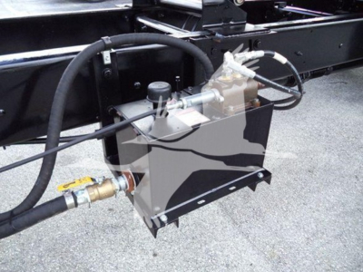 Truck undercarriage showing hydraulic control valve and reservoir with hoses and fittings.