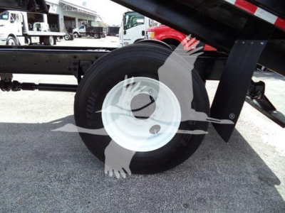 View of a truck chassis with a single large white wheel rim and black tire; part of a grapple truck; background shows other trucks.