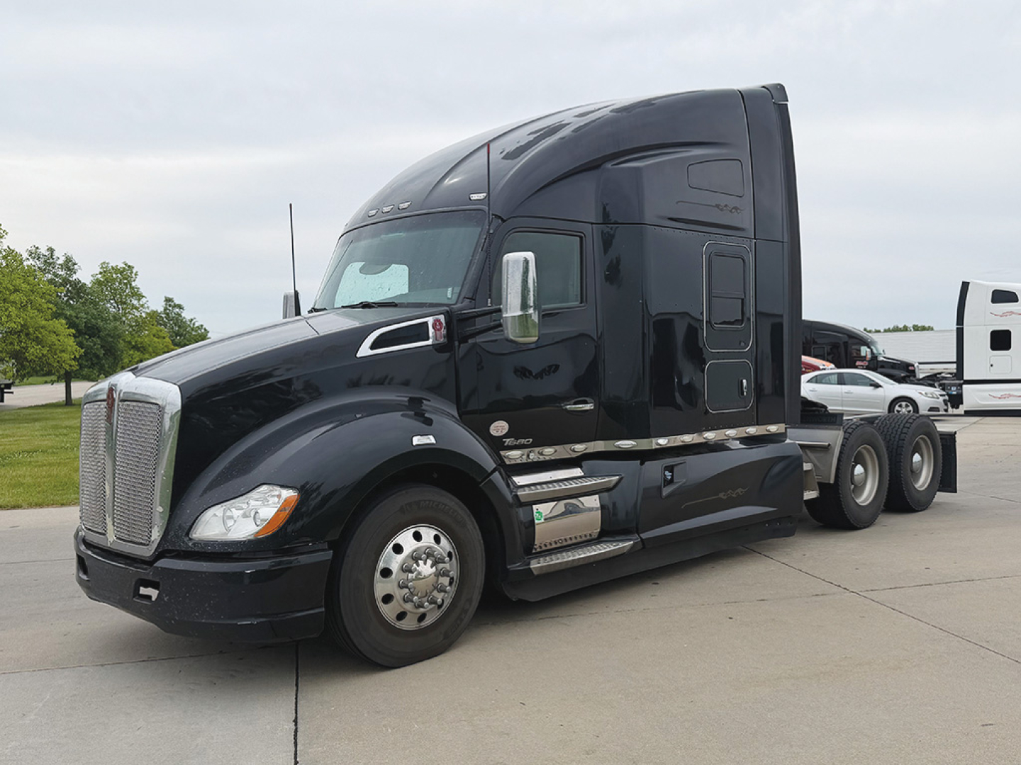 Kenworth T680 2019 conventional sleeper tractor in black parked in lot, side view showing fuel tanks, steps, and cab.