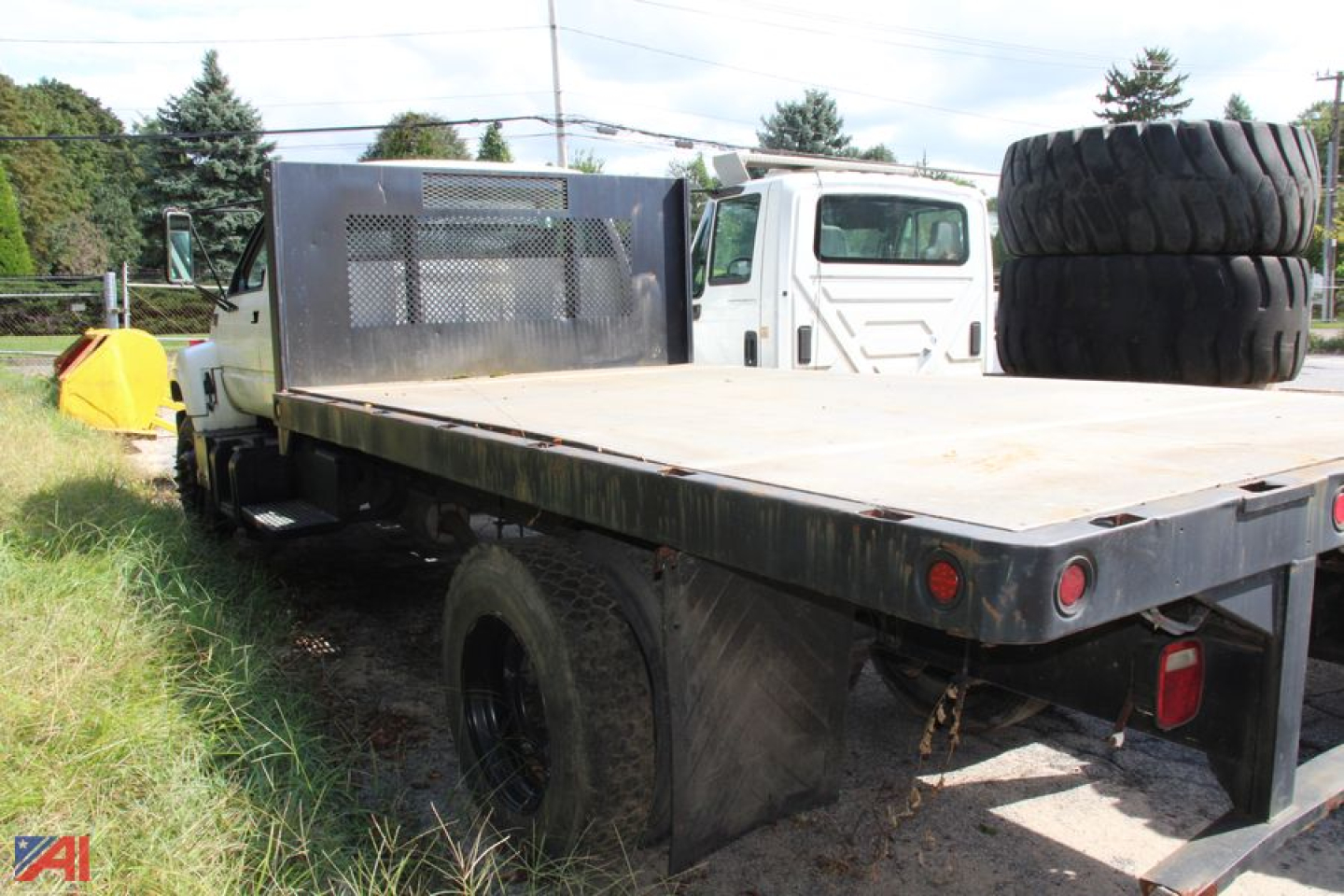 Flatbed truck with spare tire on the rear and metal cab shield, viewed from passenger side, GMC 6000 medium-duty flatbed truck.