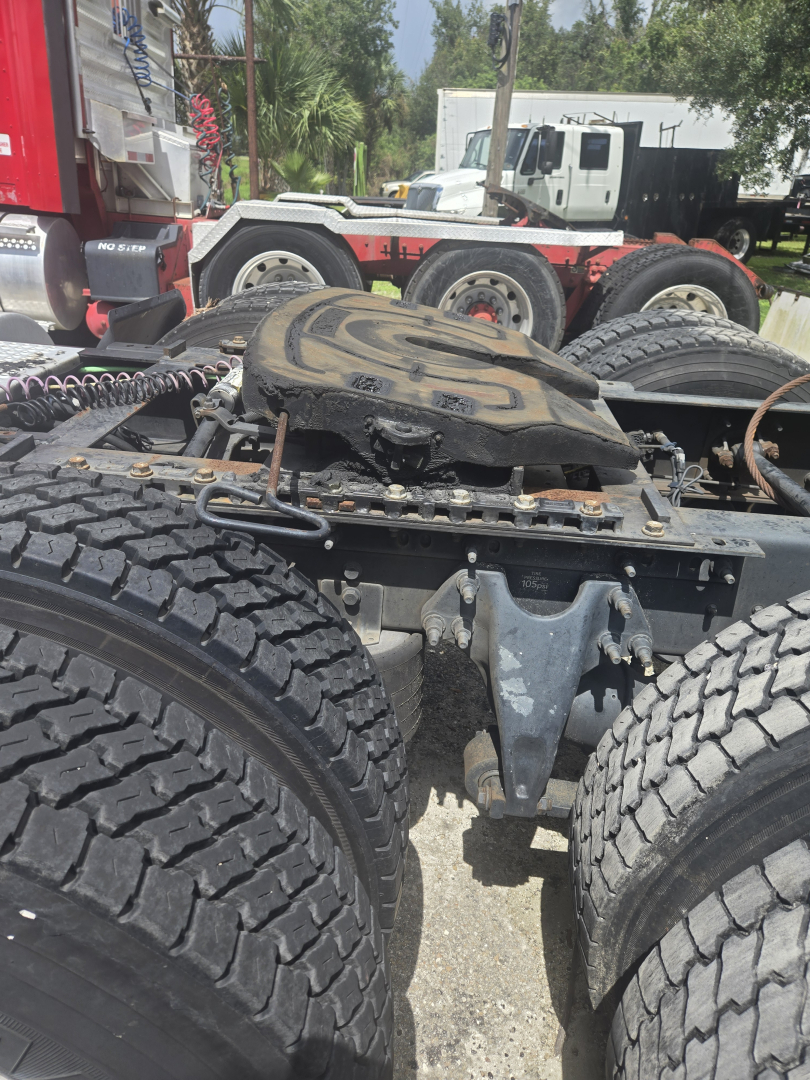 Tractor trailer fifth wheel area and rear axle set with dual rear tandems on a Freightliner day cab chassis; visible tires and hitch components in the foreground.