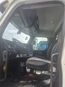 Cab interior of a 2019 Freightliner Cascadia day cab showing driver's seat, steering wheel, dashboard, and overhead console.