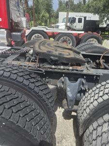Tractor trailer fifth wheel area and rear axle set with dual rear tandems on a Freightliner day cab chassis; visible tires and hitch components in the foreground.