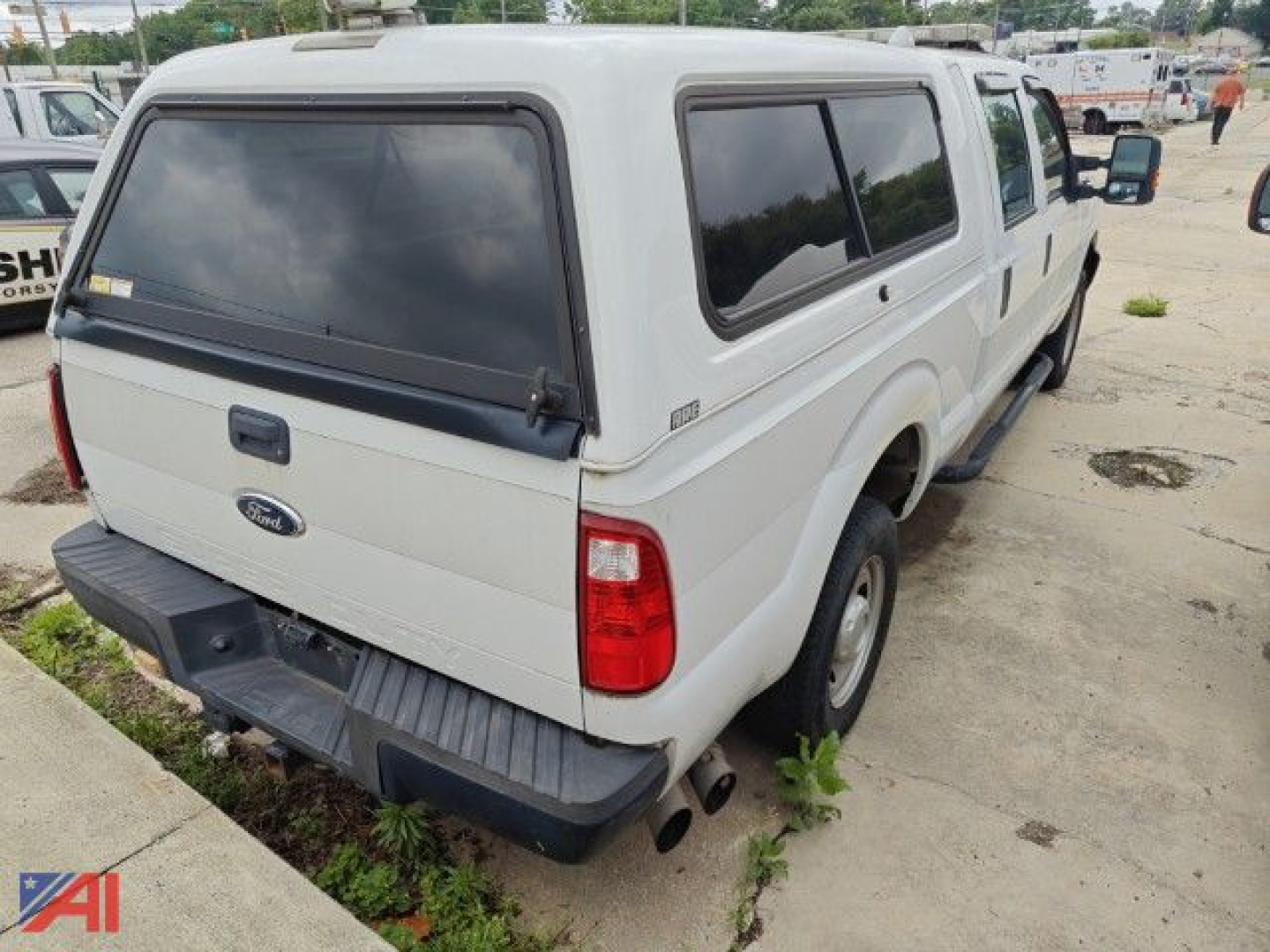 Ford F-250 crew cab pickup with white camper shell, rear view showing tailgate with Ford emblem and dual exhaust, 4x4, in a dealership lot.