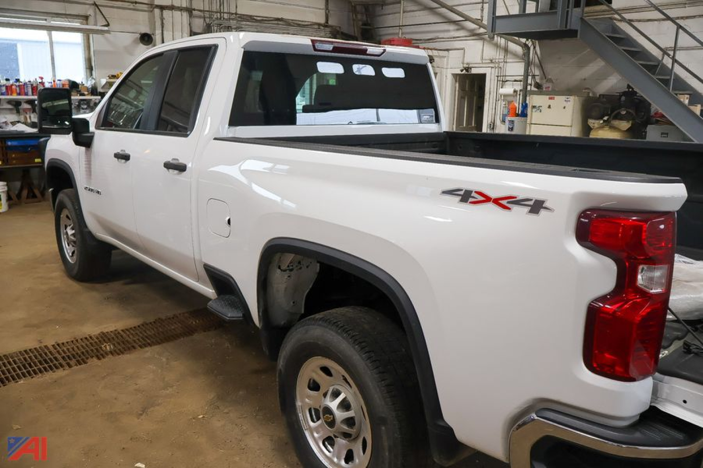 Pickup truck showing rear quarter and back of a white 2023 Chevrolet Silverado 2500HD 4x4 Crew Cab with bed cap and taillight, in a workshop.