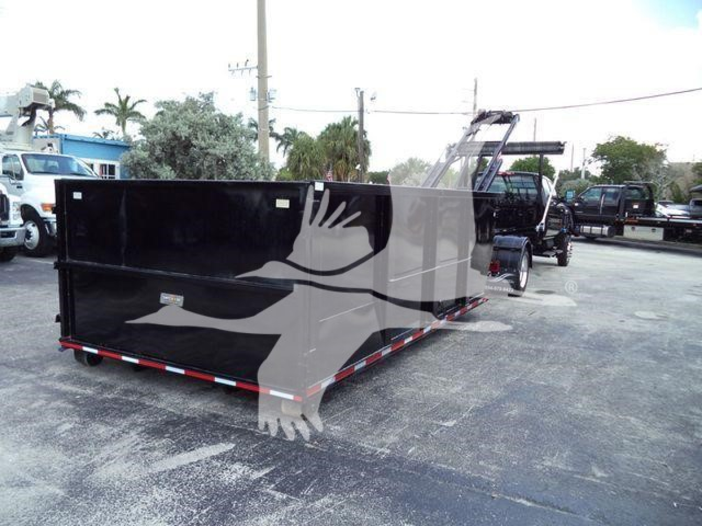 Rolloff truck in a lot showing a large black dump bed with rear ramps and reflective red/white side rails.