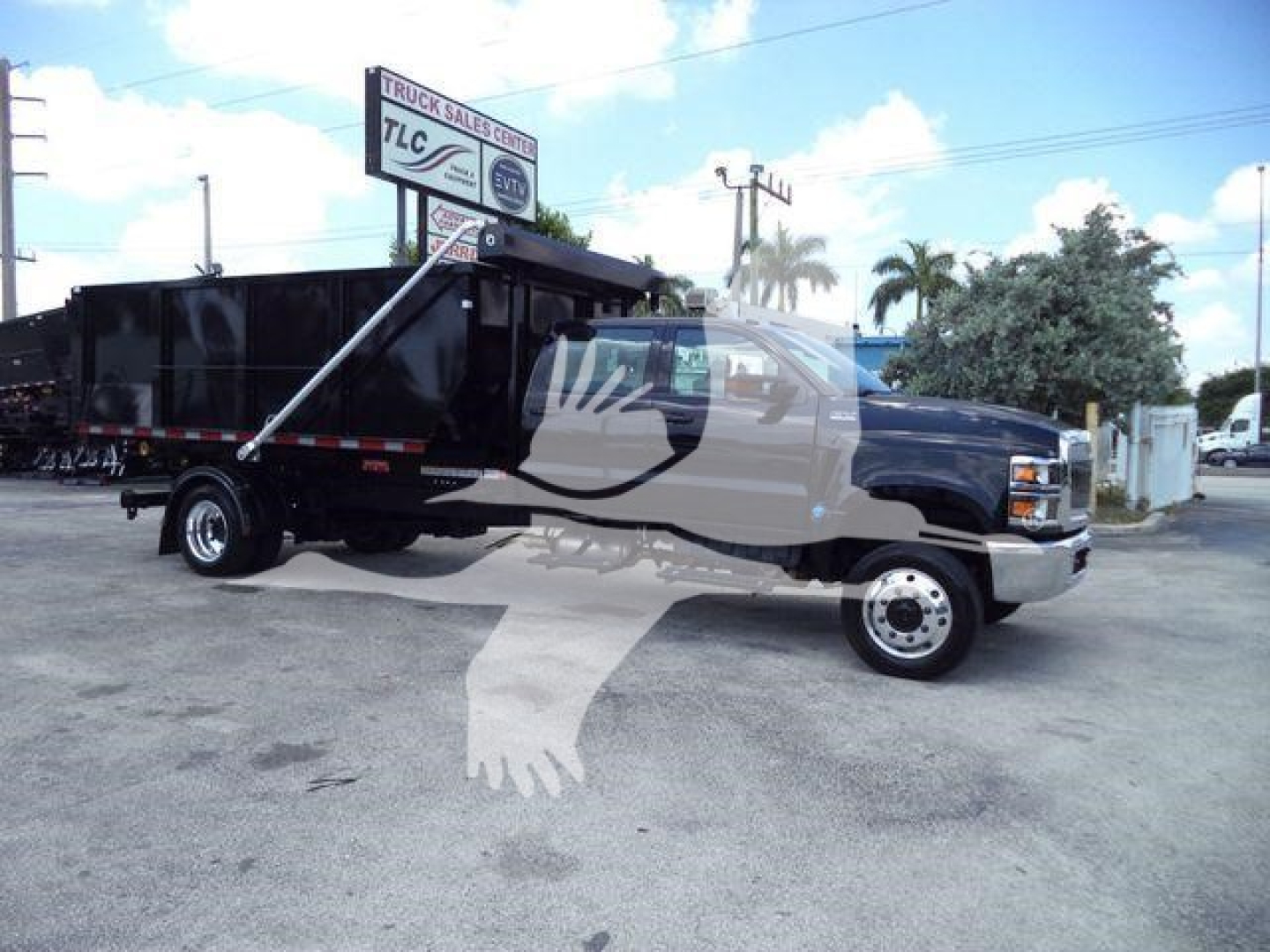 Truck shows 2023 International CV rolloff dump truck with black dump body and blue cab, side profile view, stock number CV515CREW14SNG2 visible on dealership lot.