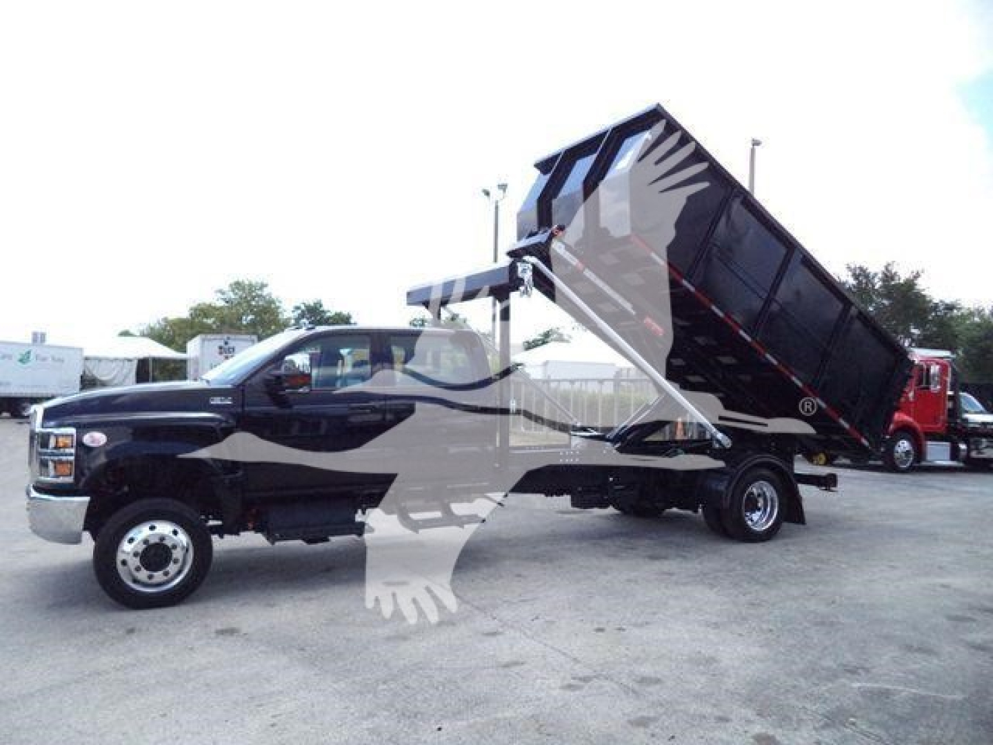2023 International CV truck in-service dump bed tilted for unloading, black cab with white wheel rims, side view showing dump bed raised.