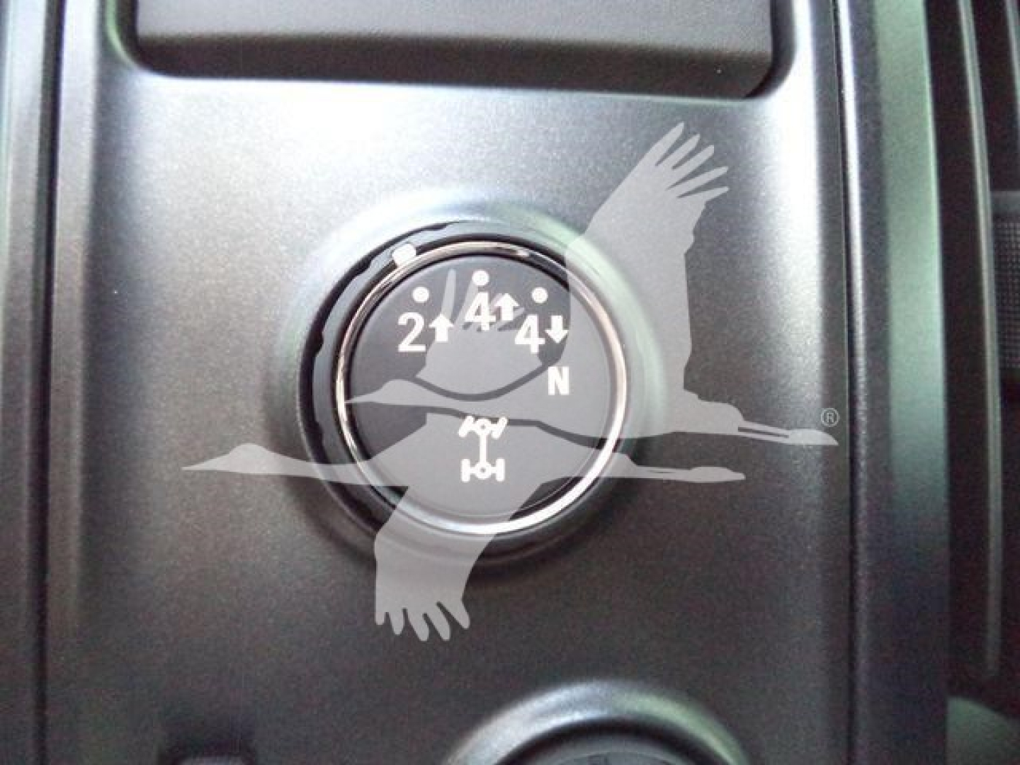 Dashboard clock or gauge with white dial showing numbers and an emblem of a bird in flight overlaying the instrument panel.