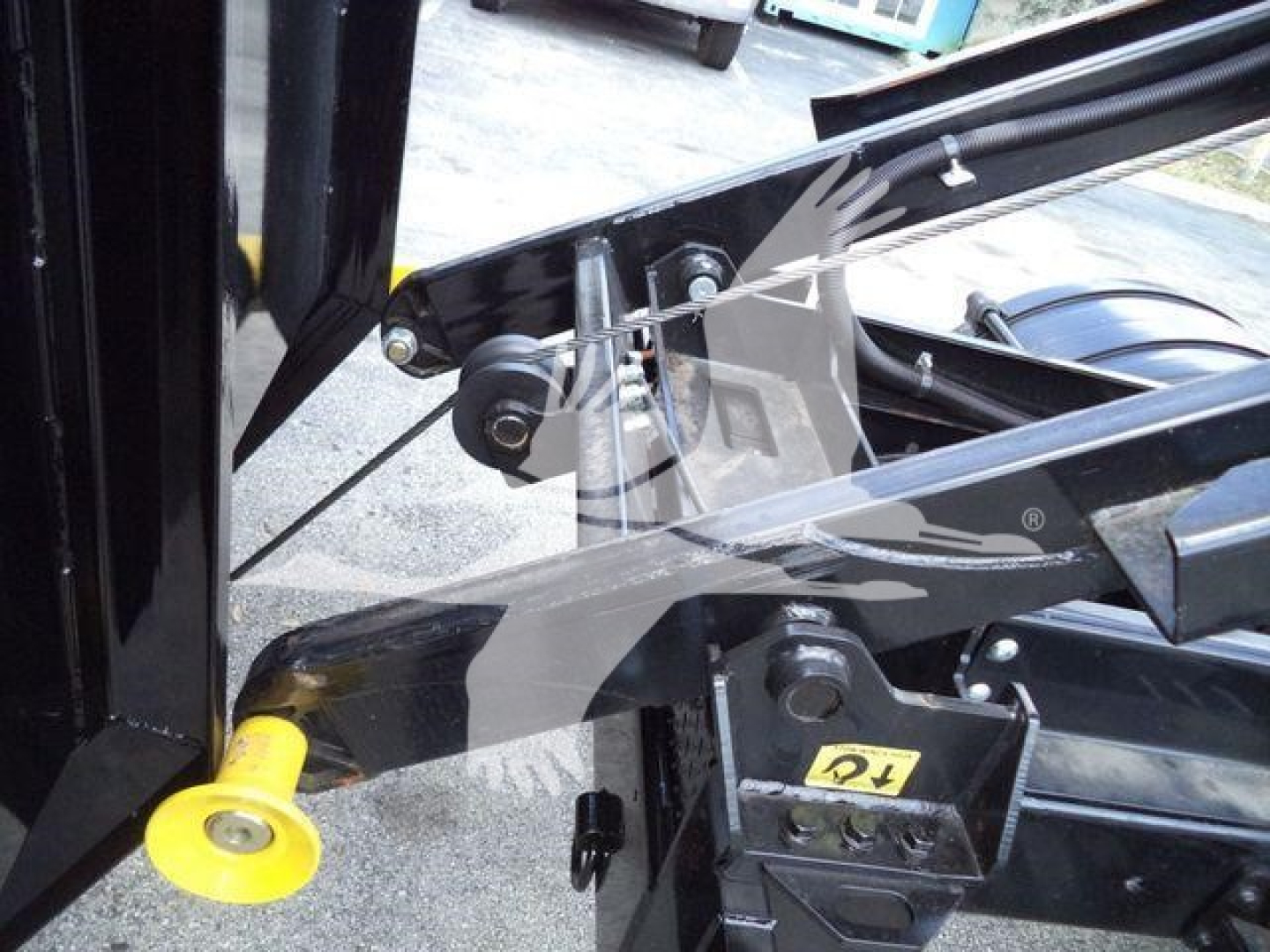 Trucks image showing hydraulic linkage and yellow pivot pin on a new 2023 International CV roll-off chassis. Visible components include black metal frame, hydraulic hoses, and a yellow accessory pin.