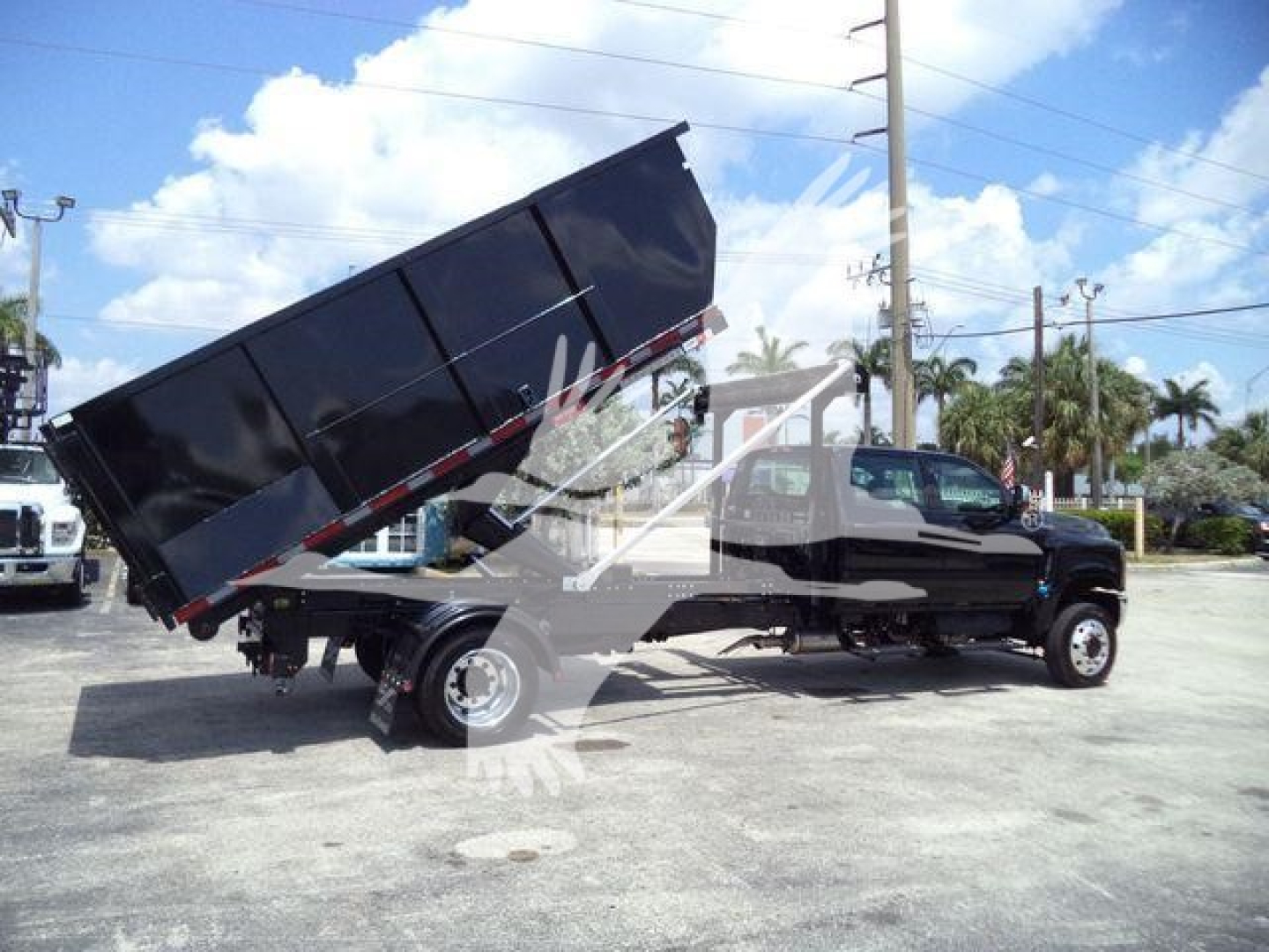 Truck with a black dump body raised at a stark angle on a heavy-duty International CV chassis, side view showing hydraulic lift and rear wheel, in a lot.