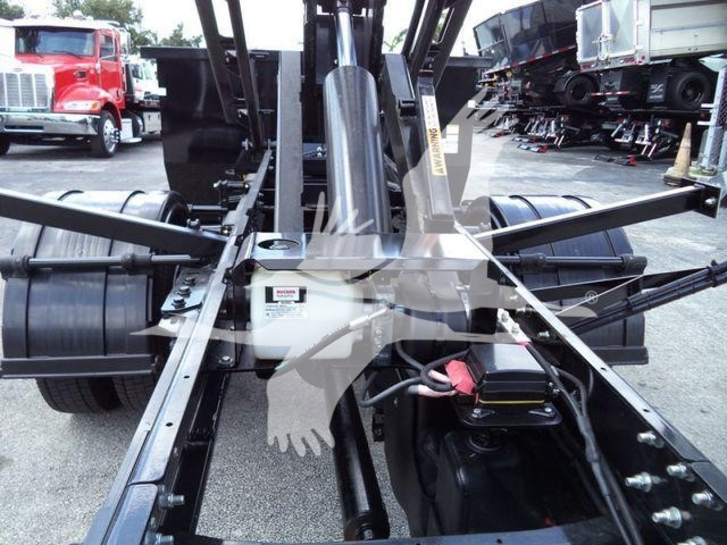 Truck chassis and hydraulic arms of an International CV roll-off truck showing the central hydraulic assembly and linkage.