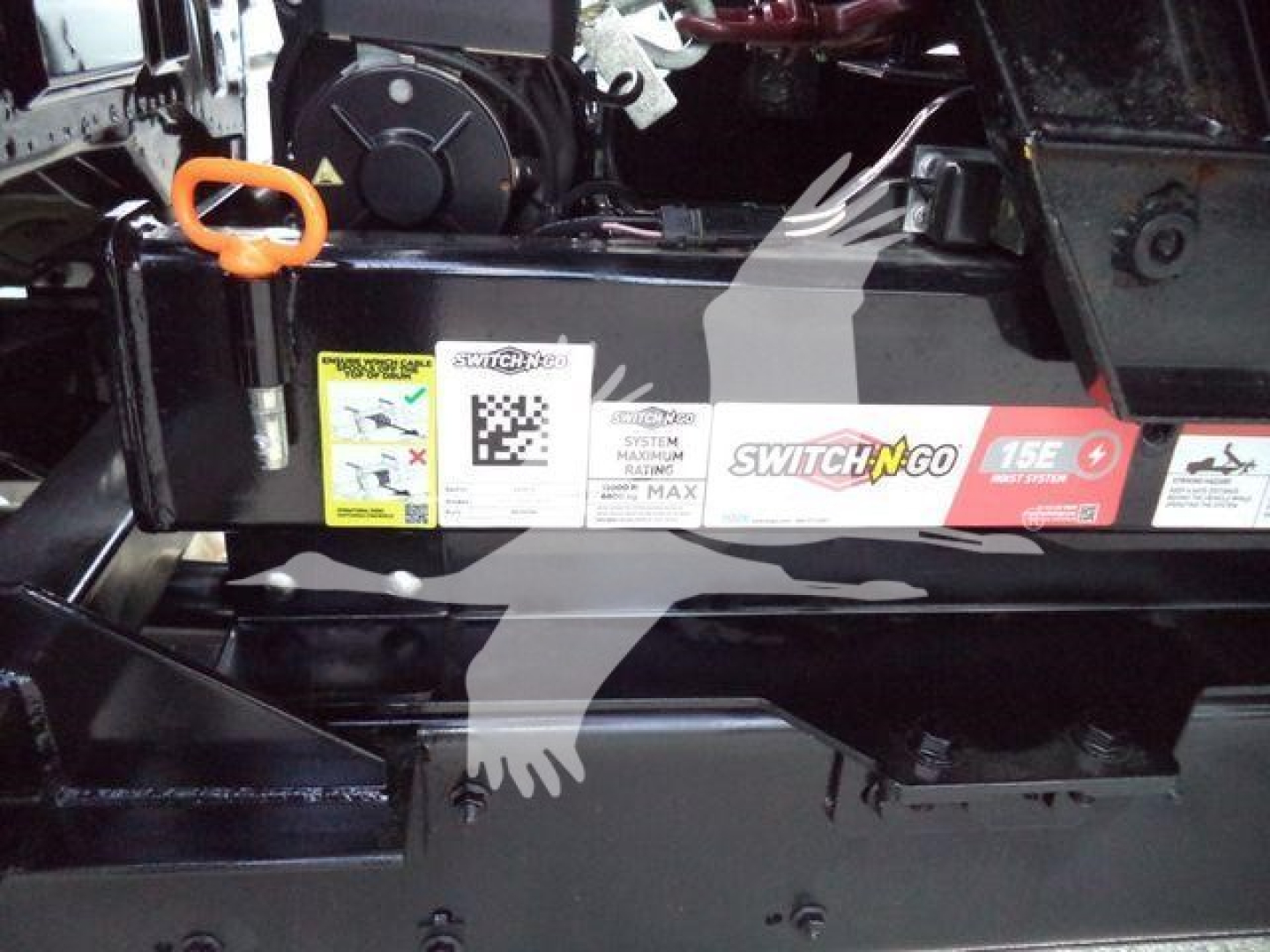 Rolloff truck chassis showing orange tow hook, warning labels, and Switch-N-Go sticker on the side rail.