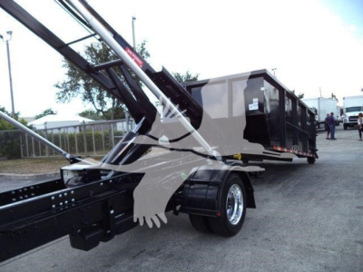 Truck chassis and roll-off hoist system with a black metal frame and a gray dump body in background, rear wheels visible.