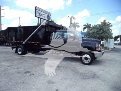 Truck shows 2023 International CV rolloff dump truck with black dump body and blue cab, side profile view, stock number CV515CREW14SNG2 visible on dealership lot.