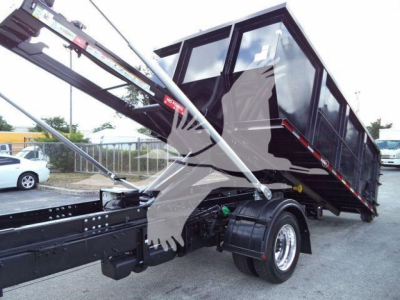 Truck bed tilted dump hopper showing hydraulic lift and black dump truck body on a heavy-duty roll-off chassis with dual rear wheels.
