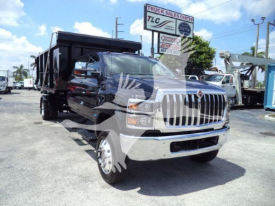 Truck front view showing 2023 International CV roll-off dump body; black cab, chrome grille, dual rear wheels, service area in background.