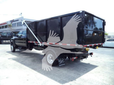 Truck bed in-vehicle view showing side and rear of black dump trailer with chained hitch and reflective tape.