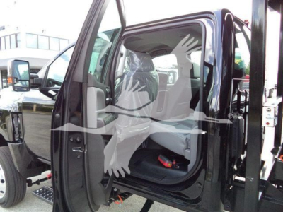 Truck cab interior visible through open driver door of a 2023 International CV roll-off truck; front bench seat, step, and side mirror visible.