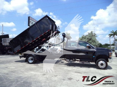 Truck with black cab and hydraulic dump bed raised in a lot, International CV series dump truck in front with load bed elevated.