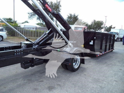 Truck deck showing long black roll-off hooklift with hydraulic arms and container in yard.