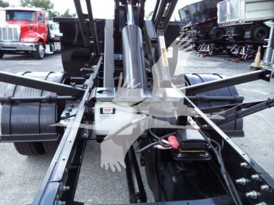 Truck chassis and hydraulic arms of an International CV roll-off truck showing the central hydraulic assembly and linkage.