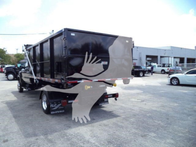 Truck-mounted roll-off dumpster trailer with black container and white graphic on side, rear view showing hitch and taillights, International CV branding not visible.