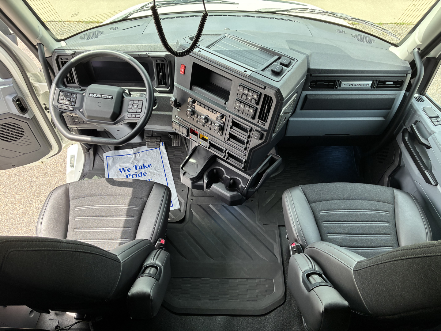 Mack PR64T76H truck cab interior showing steering wheel, dashboard, and front seats.