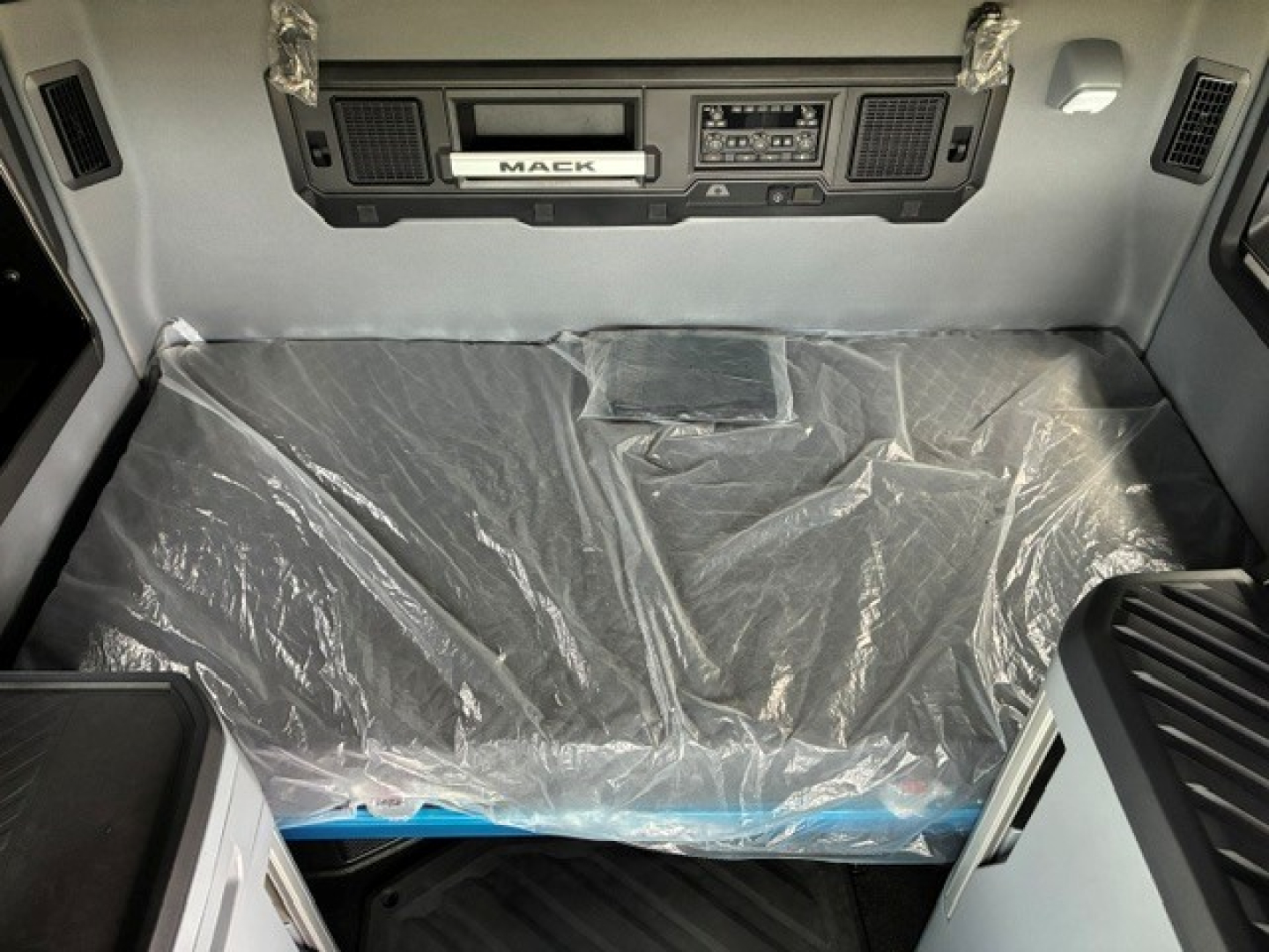 Mack PR64T76H truck cab interior showing dashboard and plastic-covered bunk area.