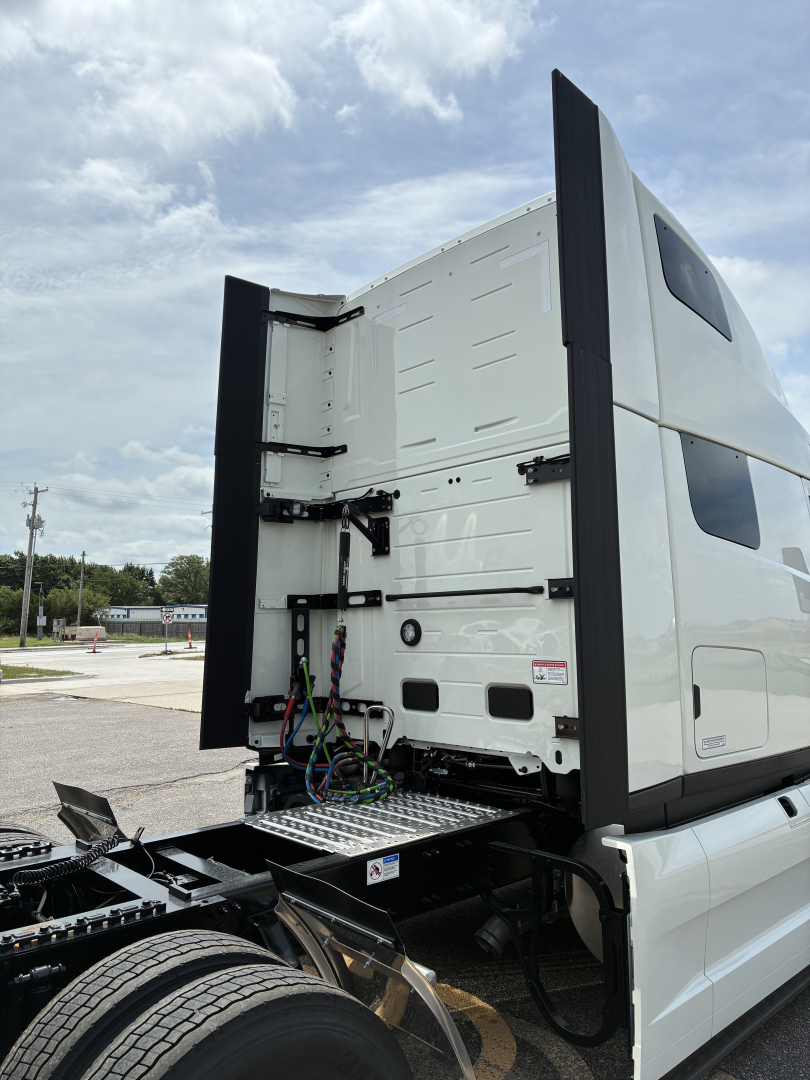 Truck cab rear showing access to sleeper; back of the cab with vertical bars and wiring beneath, chassis and dual rear wheels visible.