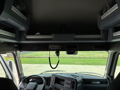 Truck cab interior front view with dashboard and overhead storage cabinets; no visible text labels legible.