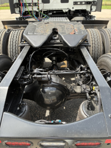 Rear view of a Mack PR64T76H tractor chassis showing drivetrain and fifth-wheel area with suspension and tires.