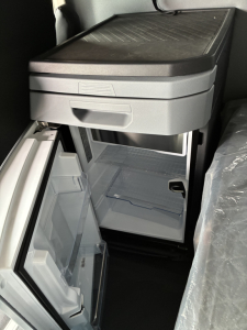 Truck cab interior showing a compact refrigerator/freezer unit with open lower drawer and shelves.