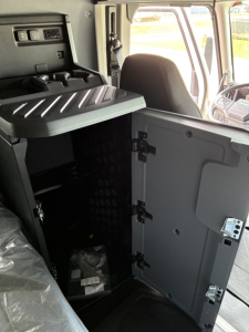 Truck cab interior showing storage cabinet with open door and latching mechanism, dashboard area visible in the background.