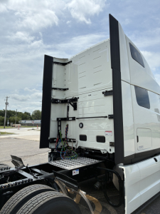 Truck cab rear showing access to sleeper; back of the cab with vertical bars and wiring beneath, chassis and dual rear wheels visible.