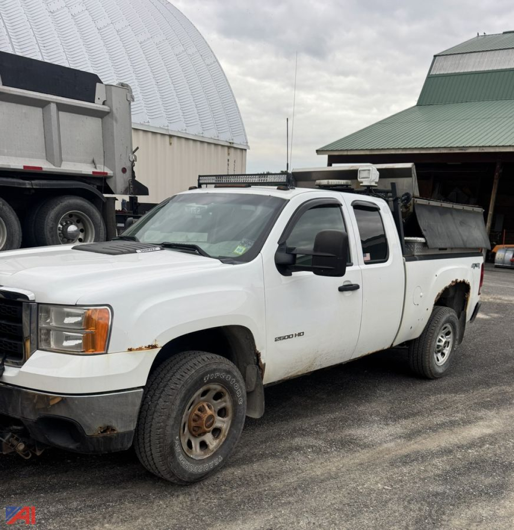GMC Sierra 2500HD extended cab pickup with plow and service bed, white, front-left view showing rust on lower fender and wheel, utility rack and equipment mounted.