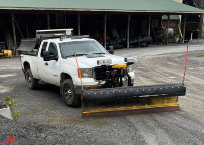 GMC Sierra 2500HD extended cab truck with plow and sand spreader in front, white cab, black plow blade, equipment yard background.